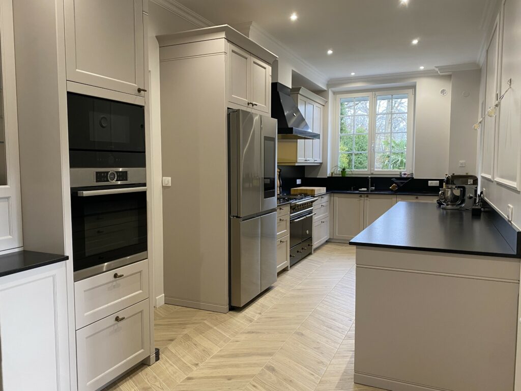 Cuisine dans un style classique beige cachemire. Plan de travail granite noir. Piano de cuisson Lacanche. Bouton de porte laiton vieilli