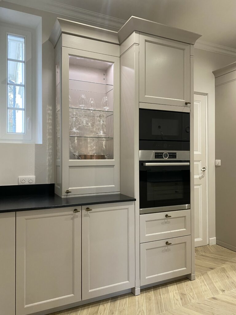 Cuisine dans un style classique beige cachemire. Plan de travail granite noir. Piano de cuisson Lacanche. Bouton de porte laiton vieilli