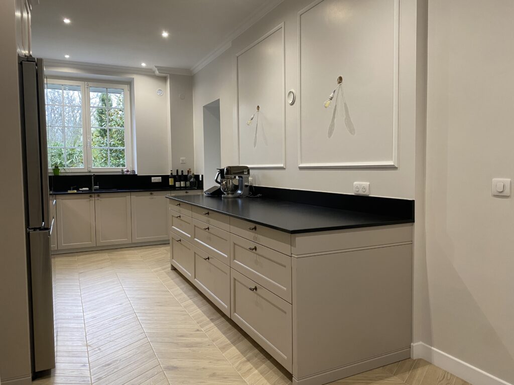 Cuisine dans un style classique beige cachemire. Plan de travail granite noir. Piano de cuisson Lacanche. Bouton de porte laiton vieilli