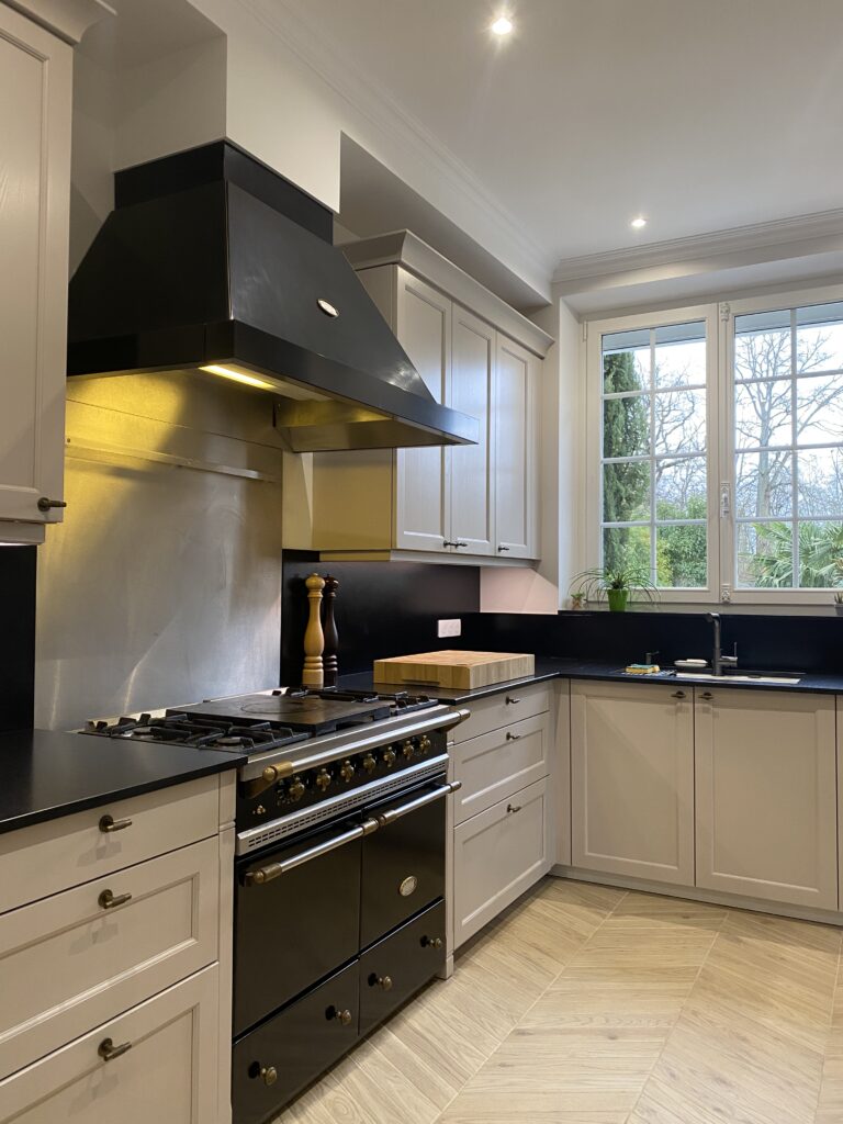 Cuisine dans un style classique beige cachemire. Plan de travail granite noir. Piano de cuisson Lacanche. Bouton de porte laiton vieilli