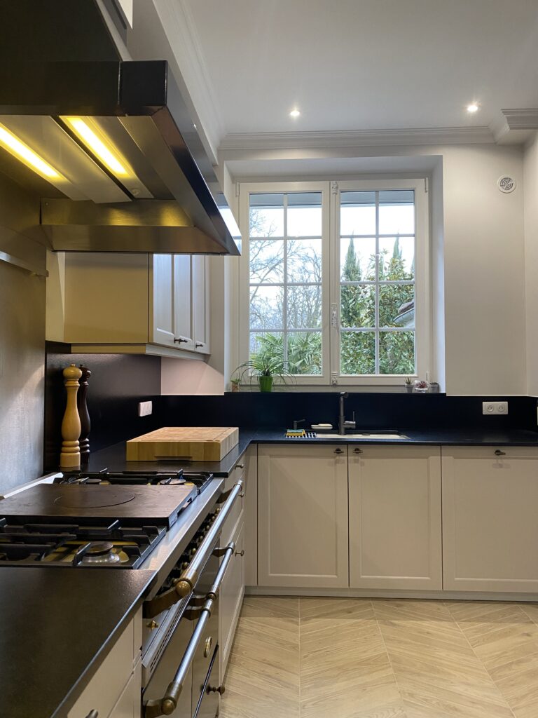 Cuisine dans un style classique beige cachemire. Plan de travail granite noir. Piano de cuisson Lacanche. Bouton de porte laiton vieilli