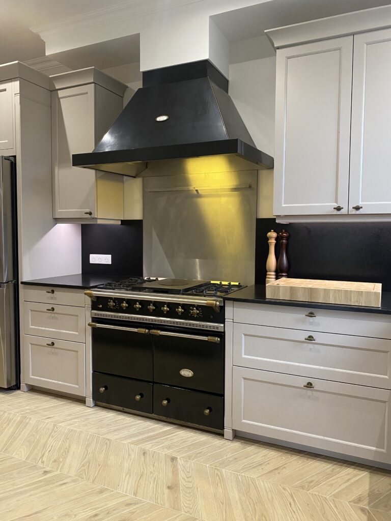 Cuisine dans un style classique beige cachemire. Plan de travail granite noir. Piano de cuisson Lacanche. Bouton de porte laiton vieilli