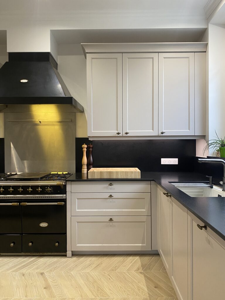 Cuisine dans un style classique beige cachemire. Plan de travail granite noir. Piano de cuisson Lacanche. Bouton de porte laiton vieilli