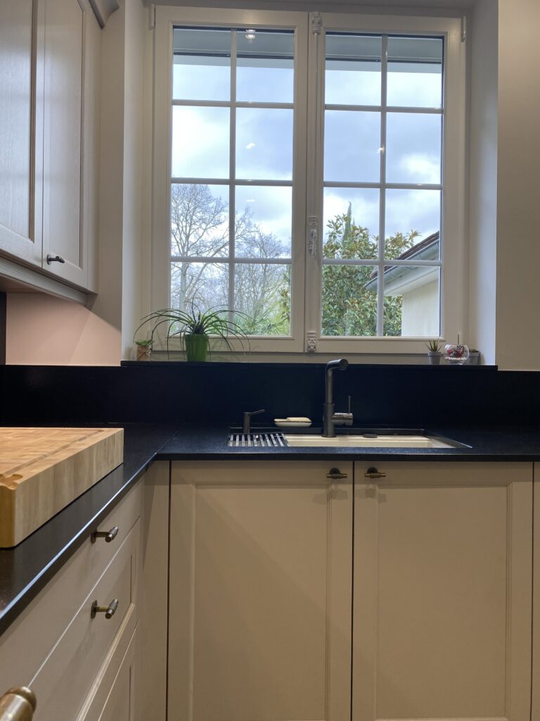 Cuisine dans un style classique beige cachemire. Plan de travail granite noir. Piano de cuisson Lacanche. Bouton de porte laiton vieilli